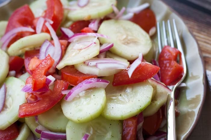 Sliced cucumbers, red onions, and tomatoes dressed with vinaigrette on a green plate with a fork