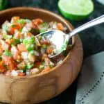 Wooden bowl filled with homemade salsa with a spoon scooping some out