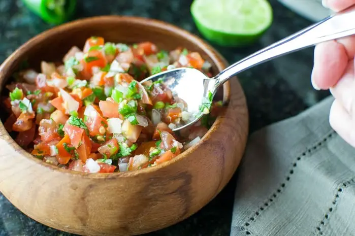 Wooden bowl filled with homemade salsa with a spoon scooping some out