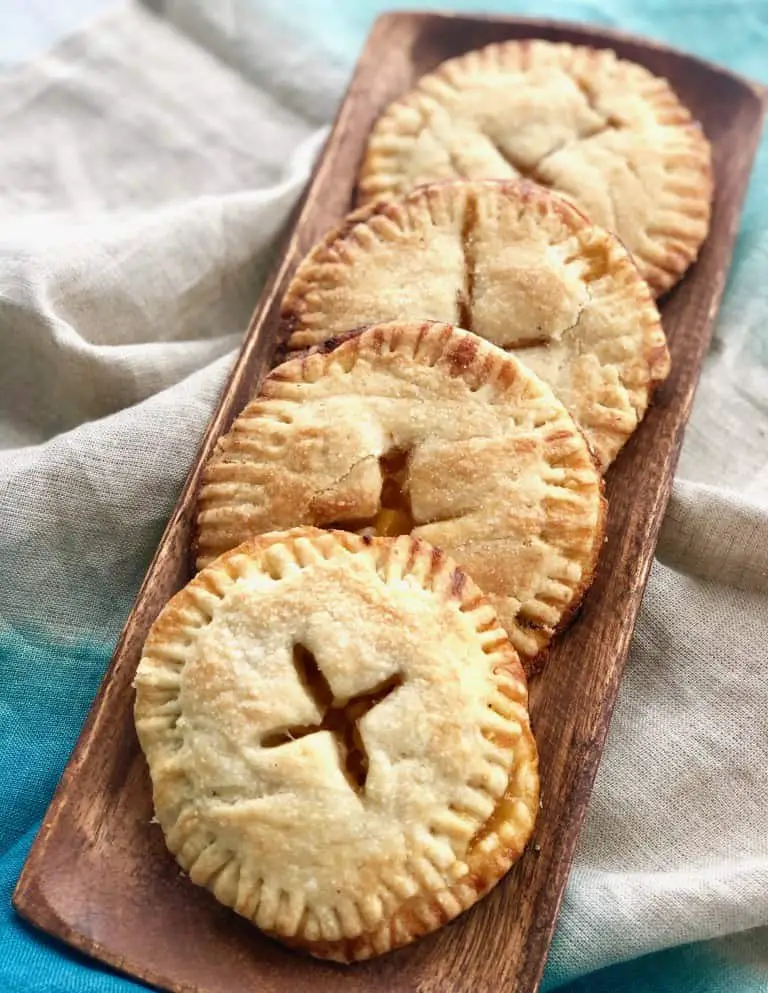 Four round peach hand pies on a wooden platter