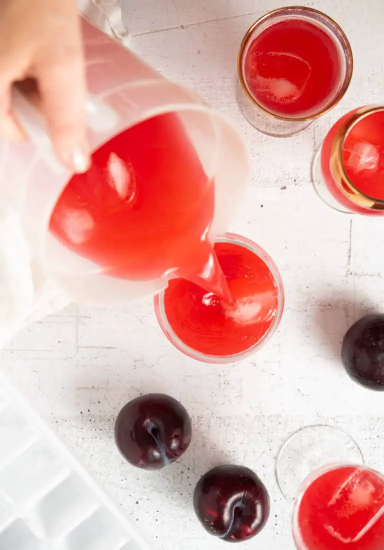 Plastic clear picture of Plum Lemonade being poured into a clear glass with ice cubes