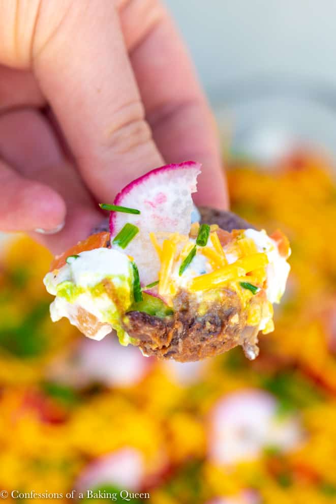 Close up of a chip holding a big bite of seven layer dip with a sliced radish on top