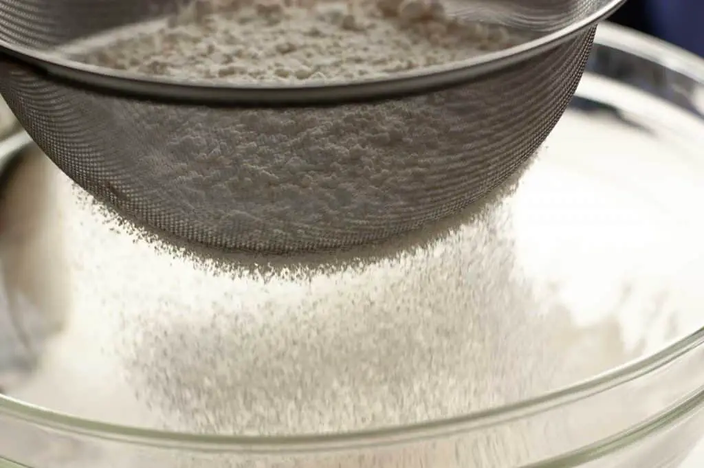 Sifting flour into a clear bowl using a fine meshed strainer