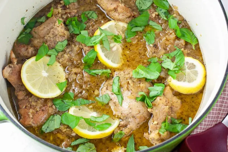 Seared chicken thighs and lemon slices with chopped basil in a green stock pot