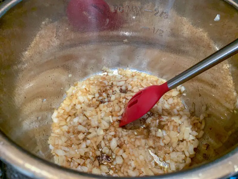 Red silicone spoon stirring onions in an Instant Pot