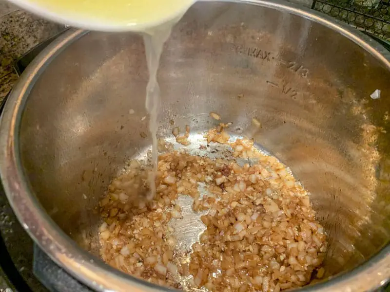 Bowl with fresh lemon juice being poured into hot pot with sauteed onions