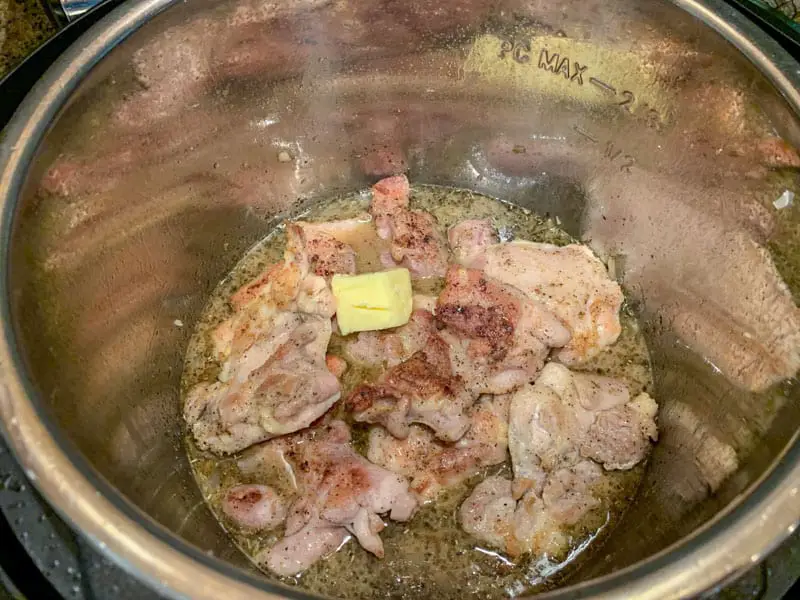 Chicken thighs in instant pot with a pat of butter on top