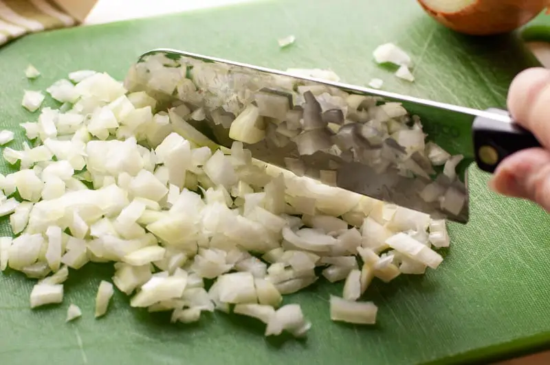 A large knife chopping onions on a green cutting board
