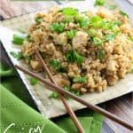 Chicken fried brown rice topped with chopped green onions on a beige plate with dark wooden chopsticks