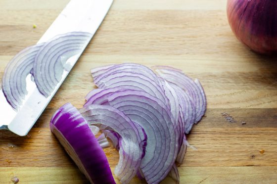 Thinly sliced red onions on a wooden cutting board