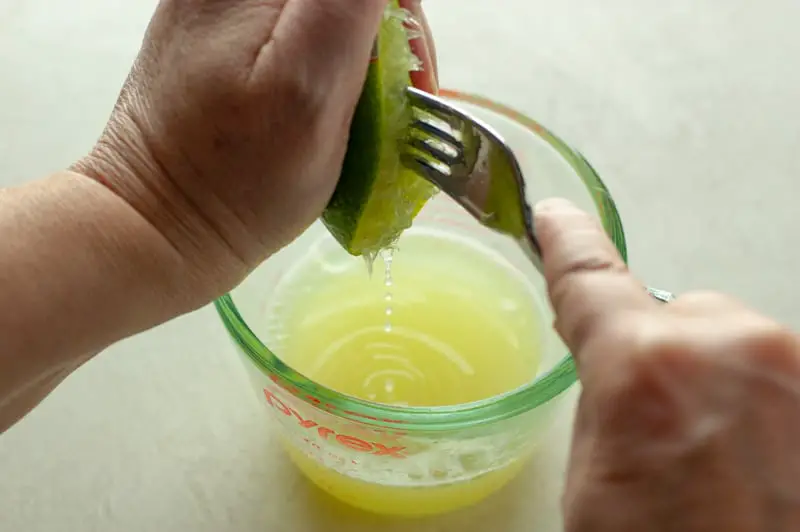 Showing the process of squeezing lime juice into a measuring up using a fork