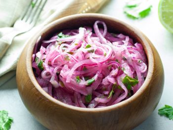 brown wooden bowl filled with thinly sliced marinated red onions