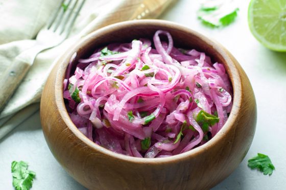 brown wooden bowl filled with thinly sliced marinated red onions