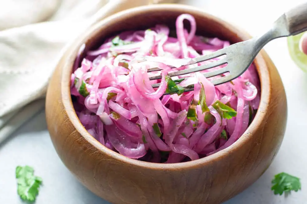 red onions in a wooden bowl that have turned pink from marinating