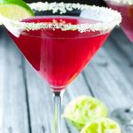 Cranberry and vodka in a clear martini glass with sugary green crust around the rim with text Cape Cod Cosmo with Sugar Lime Rim