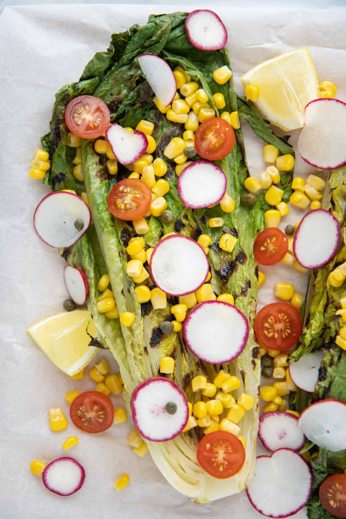 Head of grilled romaine lettuce topped with corn, radishes, and tomatoes