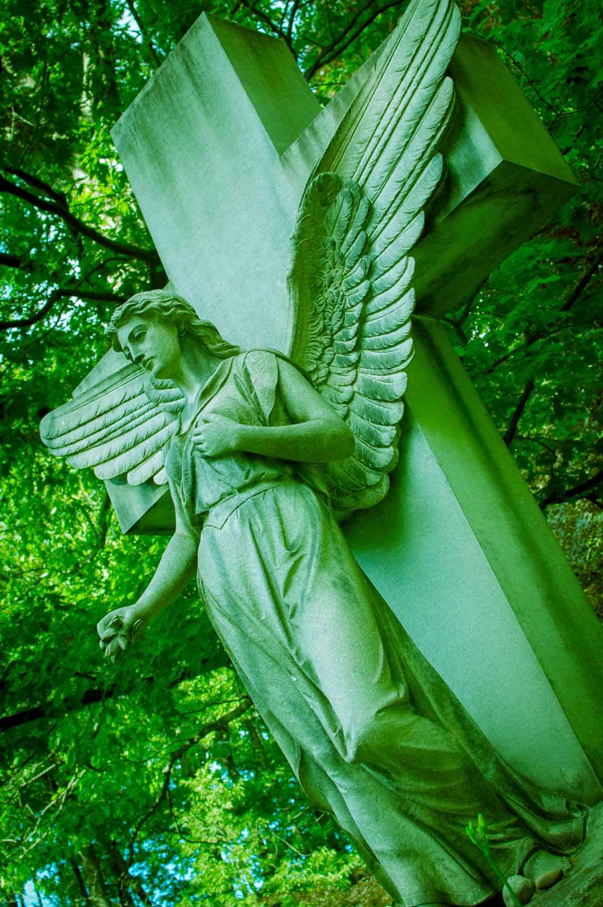 Cement cross and angel statue in a forest